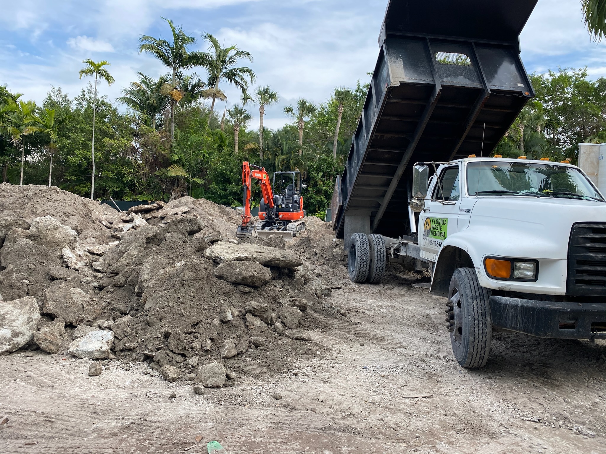 Excavator loading construction and demolition debris into a dump truck on a South Florida job site